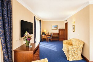 A hotel room with a bed, a desk, a chair, a television, a lamp, and a painting on the wall.
