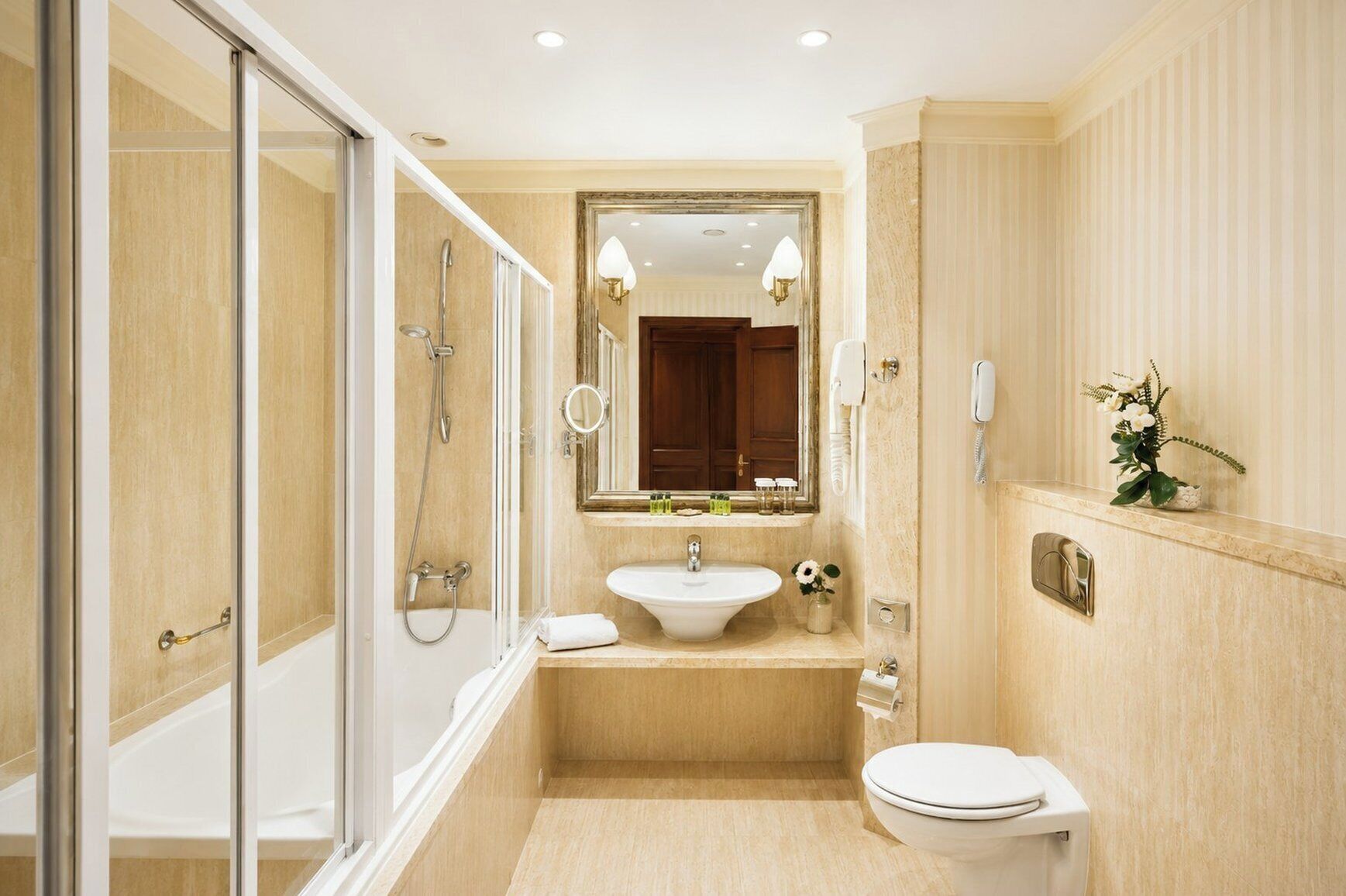 A bathroom with a glass shower enclosure, a sink with a mirror, a toilet, and a small plant on the countertop.