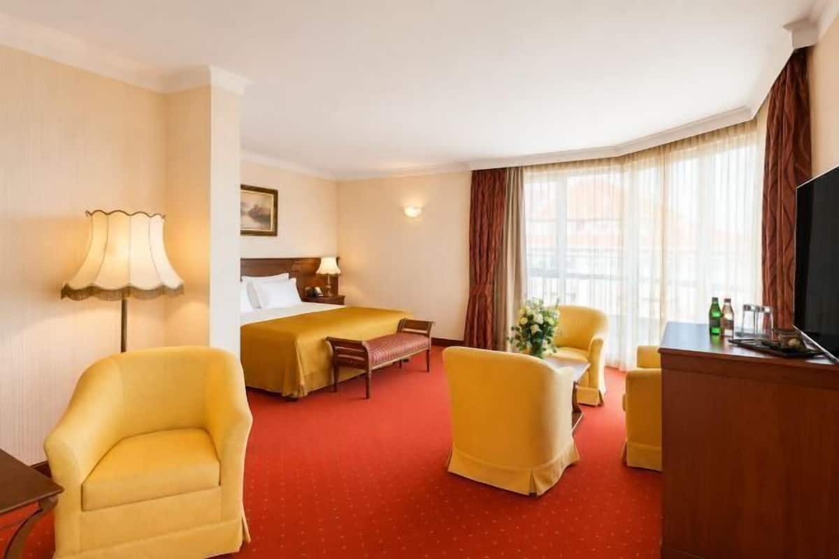 A hotel room with a bed, two armchairs, a desk, a television, and a window with curtains.