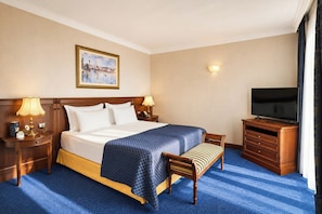 Habitación de hotel con cama, lámparas de noche, televisión, un banco de madera y un cuadro en la pared.