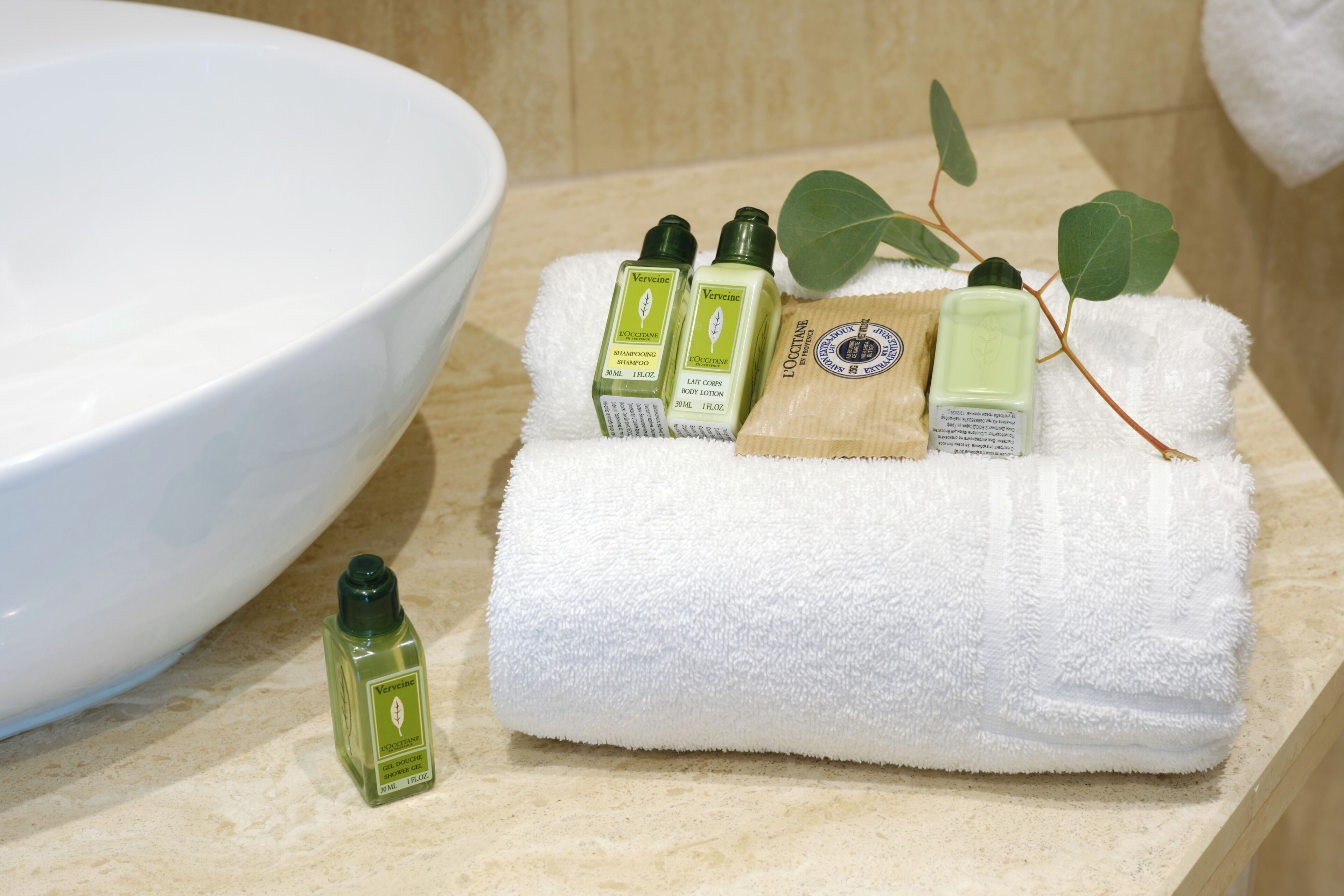 Un baño con un lavamanos blanco, una toalla blanca y botellas de jabón líquido y loción verde.
