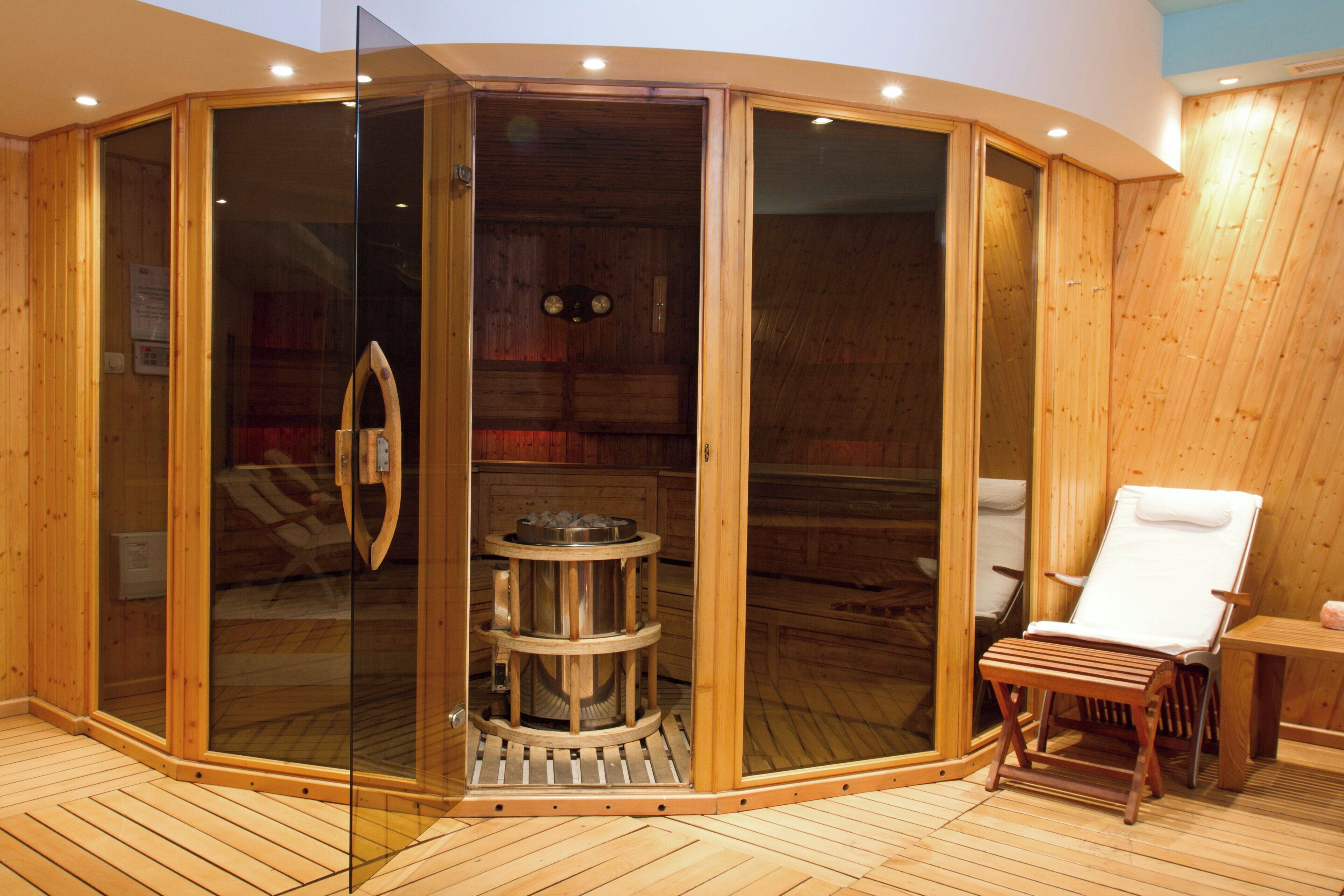 A sauna room with a wooden interior, a glass door, a wooden bench, and a white chair.