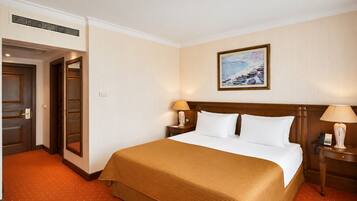 A hotel room with a bed, two bedside tables, a painting on the wall, and a door.