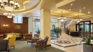 A spacious lobby with a grand staircase, elegant furniture, and a chandelier.