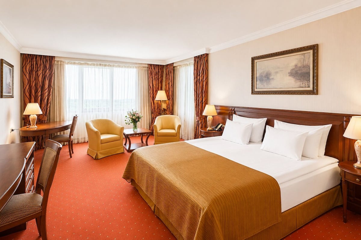 A hotel room with a large bed, two armchairs, a desk, and a dining table.