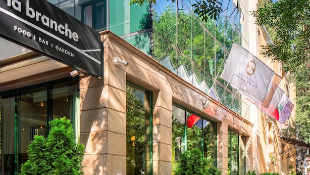 A building facade with a sign for 'la branche' food, bar, and garden. There are potted plants and a flag with the Crystal Palace Sofia logo.