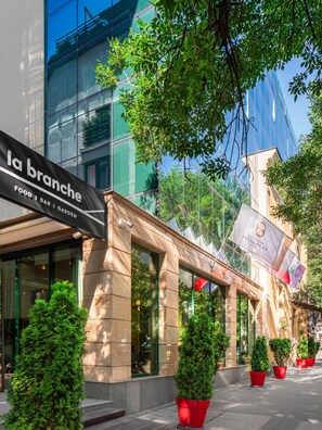 A building facade with a sign for 'la branche' food, bar, and garden. There are potted plants and a flag with the Crystal Palace Sofia logo. - Crystal Palace Boutique Hotel (Sofia)