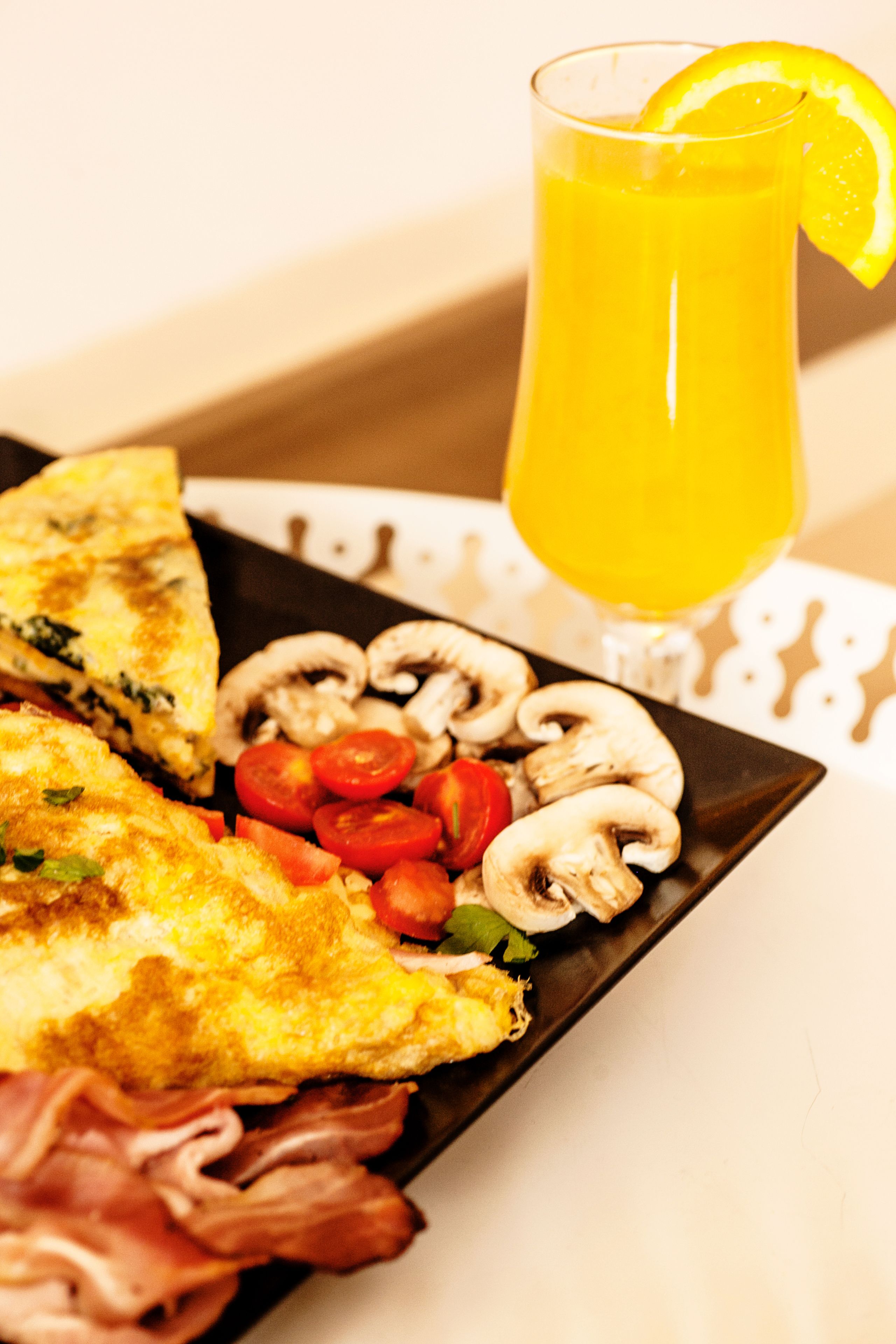 Un plato de desayuno con tortilla, champiñones, tomates y tocino, además de un vaso de jugo de naranja.