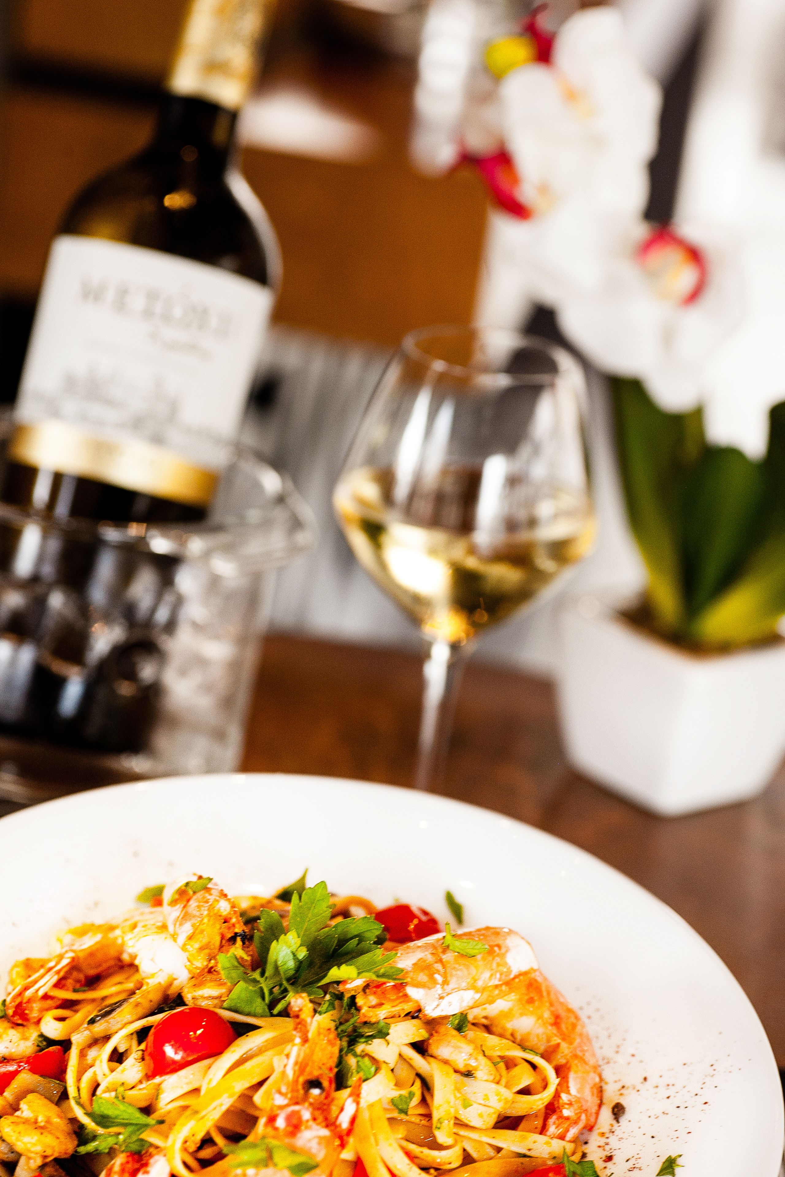 A plate of pasta with shrimp, a bottle of wine, and a glass of white wine on a table.