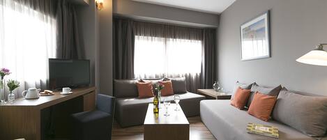 Una sala de estar moderna con un sofá, una mesa de centro y un televisor. Hay cortinas, un jarrón con flores y un cuadro en la pared.