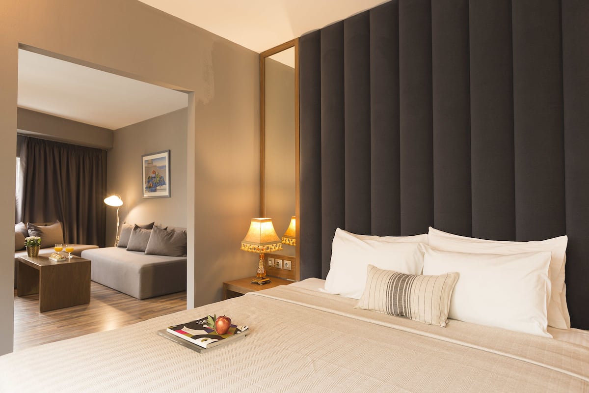 A hotel room with a large bed, a bedside table with a lamp, a sofa, and a mirror.