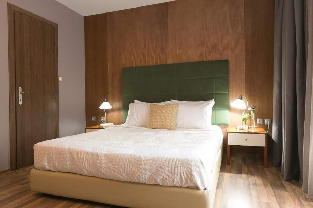 A hotel room with a large bed, wooden panel walls, a green headboard, two bedside tables with lamps, and a door.