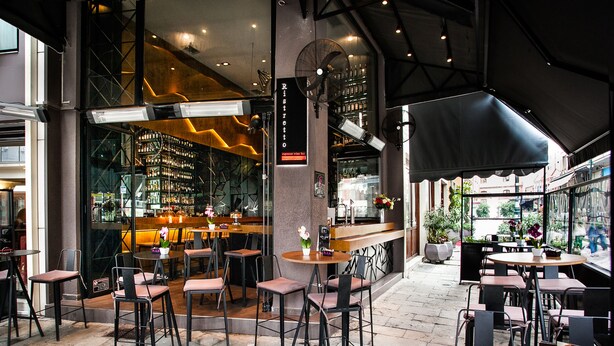 A restaurant with outdoor seating, a bar area, and a view of the street.