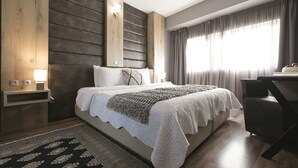 A modern bedroom with a large bed, a desk, and a window with curtains.