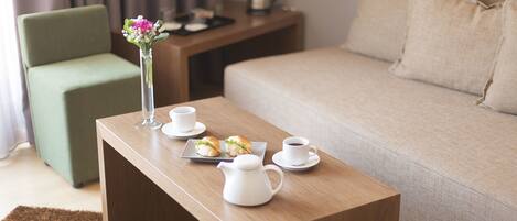 A neatly arranged room with a wooden coffee table, a green armchair, a beige sofa, and a small side table with a vase of flowers and a kettle.