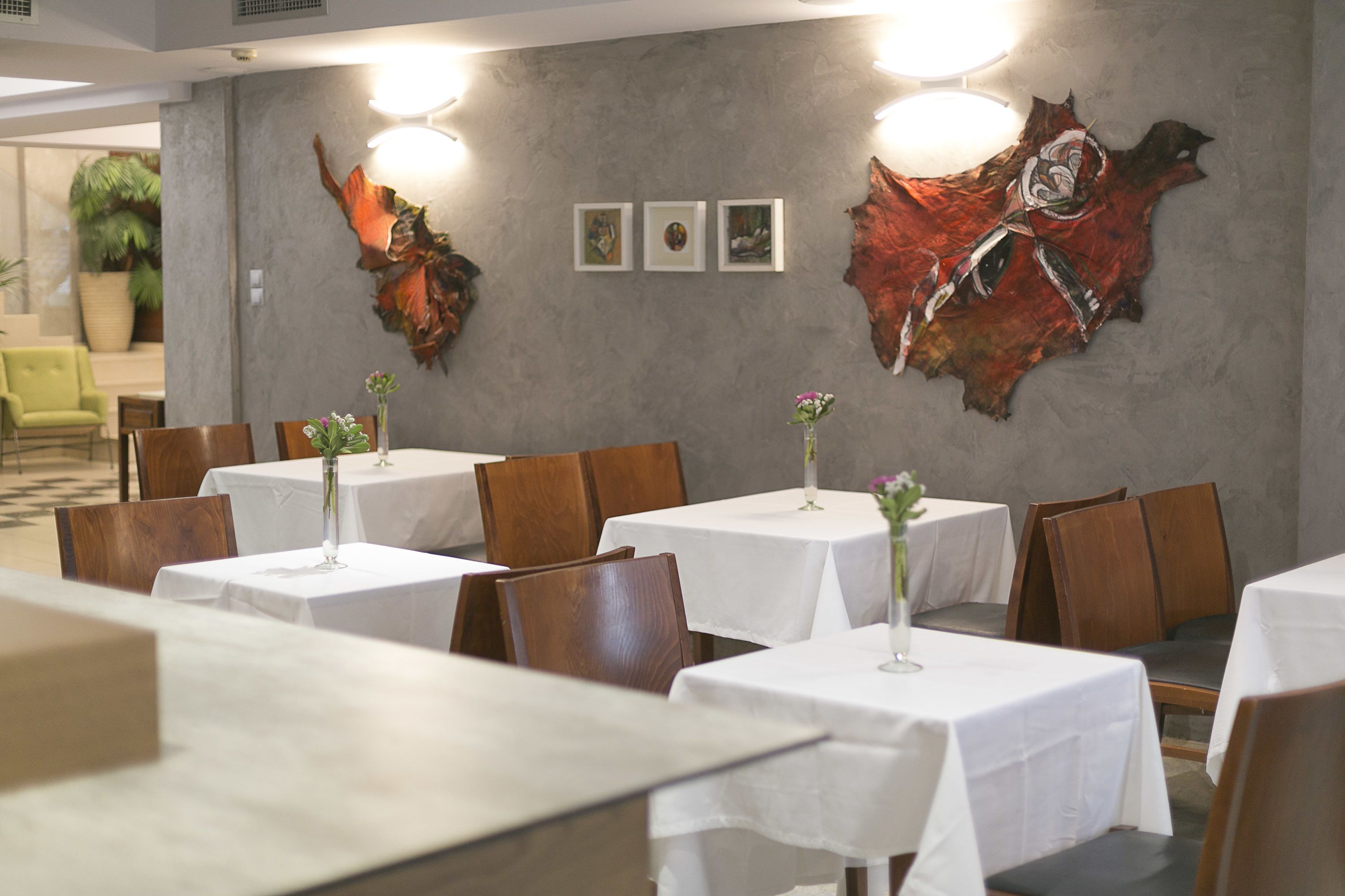 Un restaurant où les tables sont recouvertes de nappes blanches, où les chaises sont en bois et où des œuvres d’art sont accrochées aux murs.