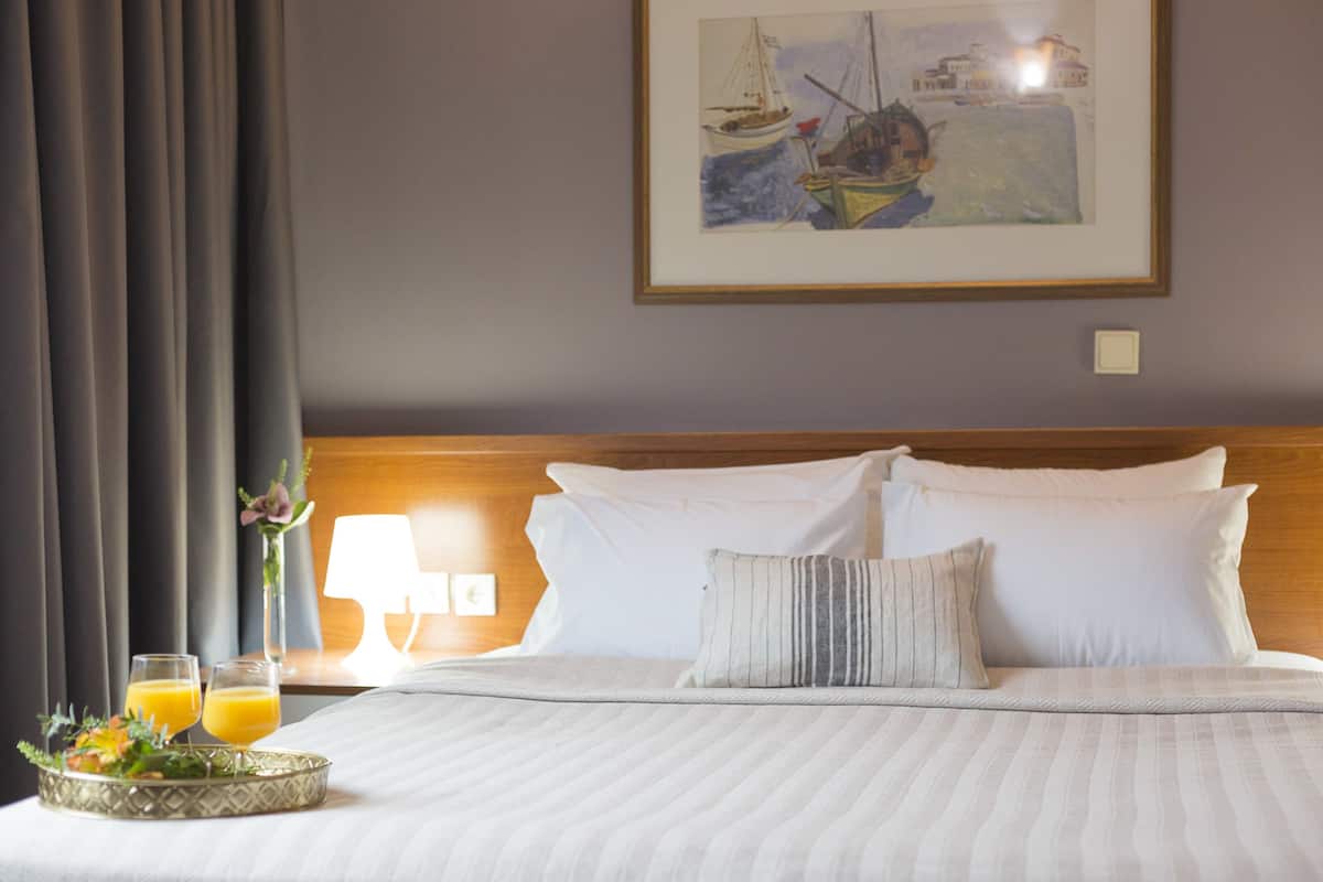 A neatly made bed with white linens, a framed painting above it, and a tray with two glasses of orange juice on the side.
