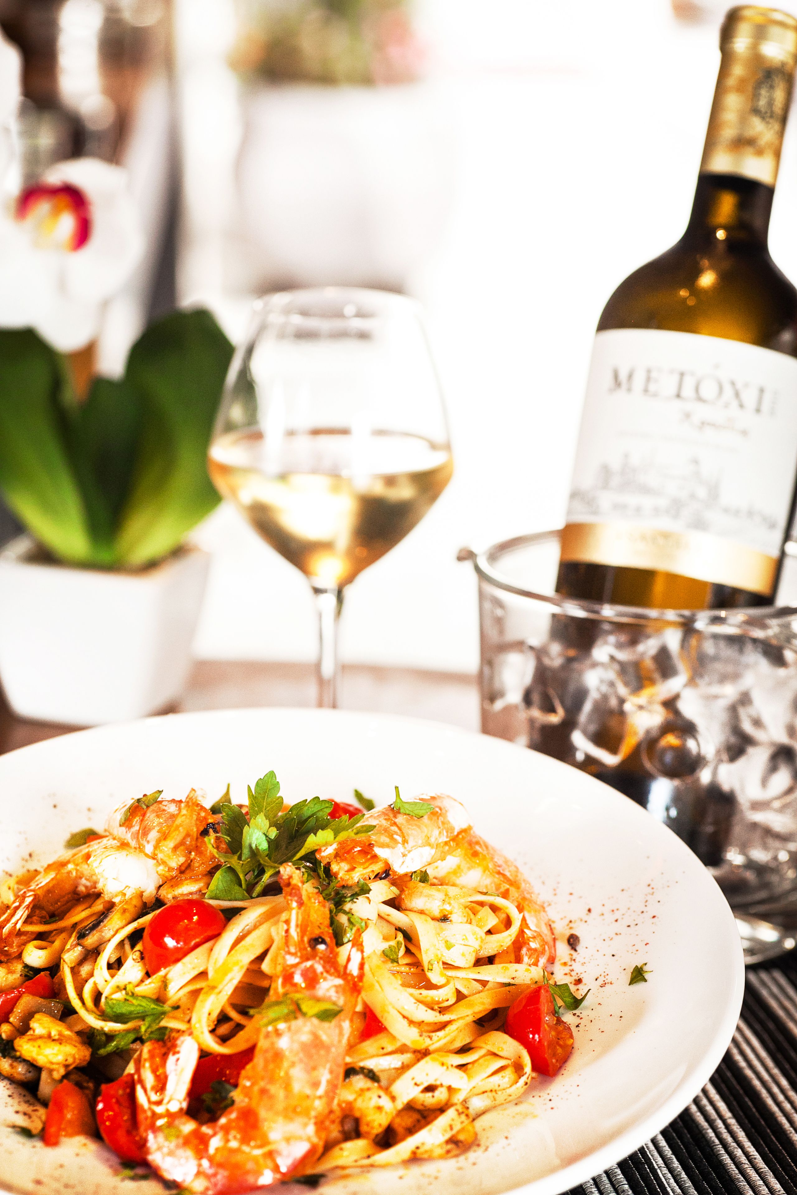A plate of pasta with shrimp, a glass of white wine, and a bottle of wine in the background.
