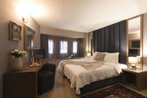 Una habitación de hotel moderna con una cama grande, un escritorio con un florero y copas de vino, un espejo y vistas al exterior a través de la ventana.