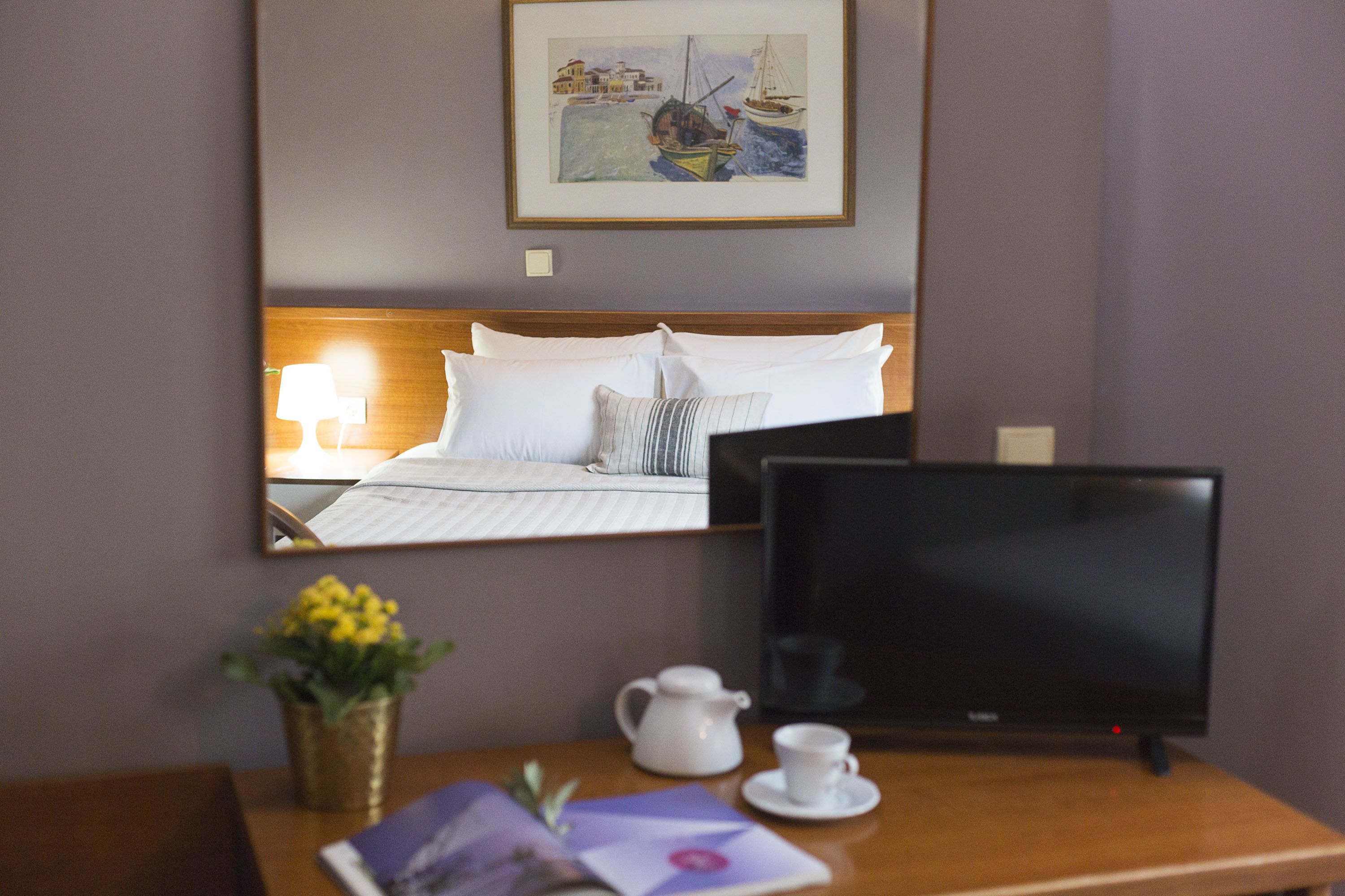 Een hotelkamer met een bed, een televisie, een nachtkastje met een lamp, een vaas met bloemen en een ingelijst foto aan de muur.