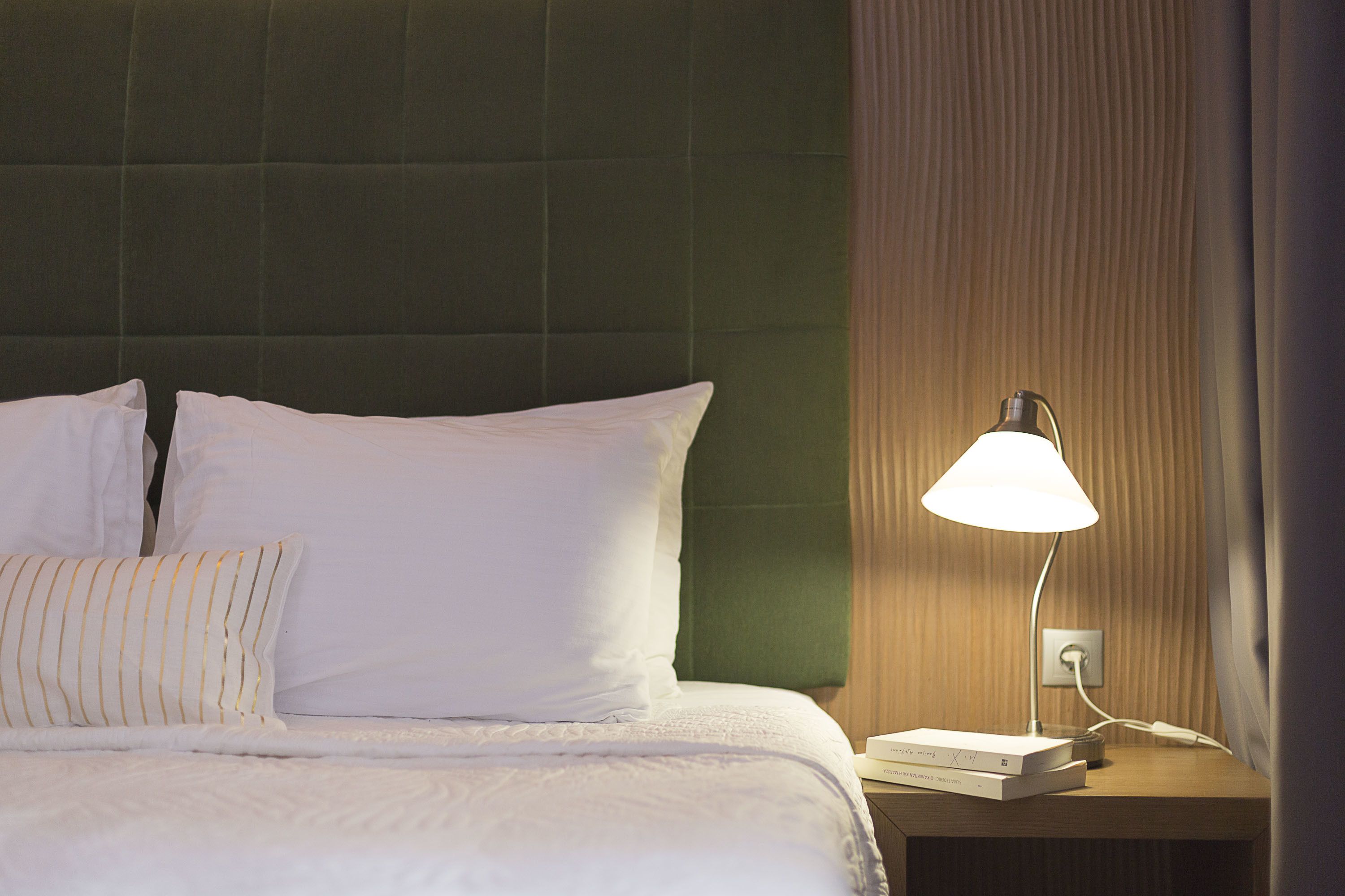 Una cama bien hecha con sábanas y almohadas blancas, una lámpara de noche y un libro en la mesita.