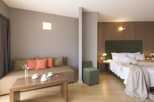 Quarto de hotel com sofá, cama, mesa de cabeceira com luminária e pequena mesa com vaso e bules.