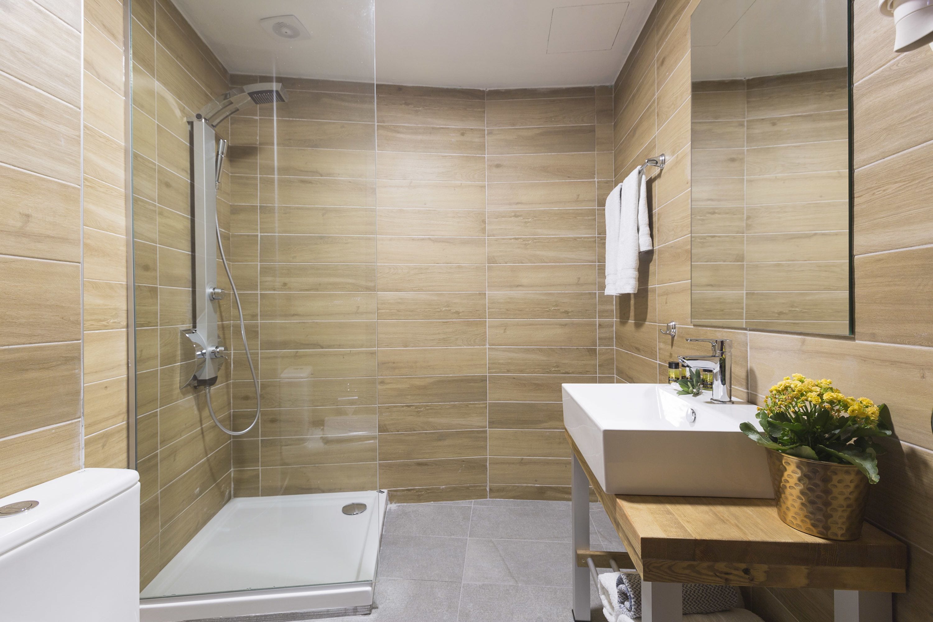 Un baño moderno con cabina de ducha de vidrio, un lavamanos blanco y un tocador de madera.