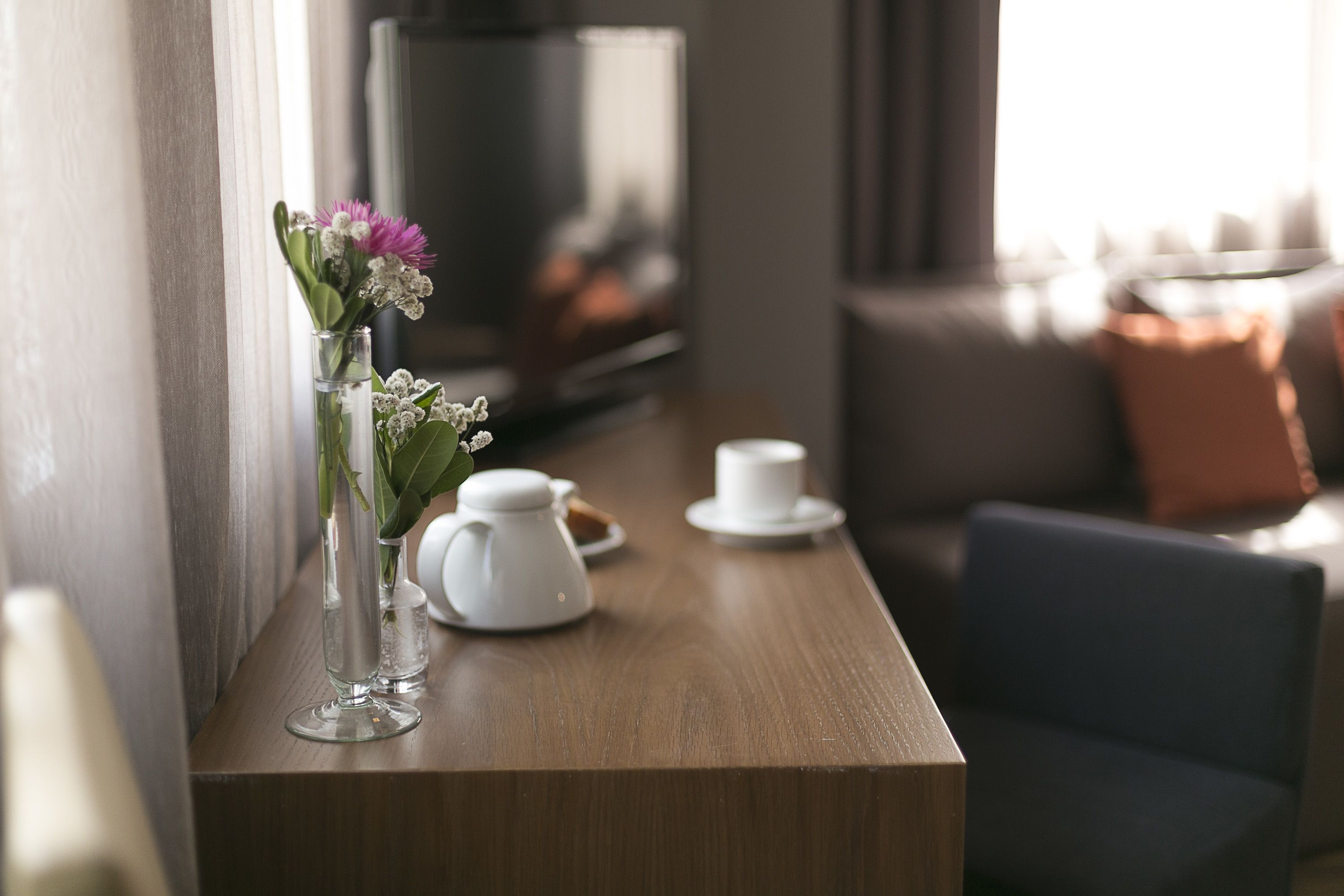 A wooden table with a white teapot, a cup, and a vase with flowers.