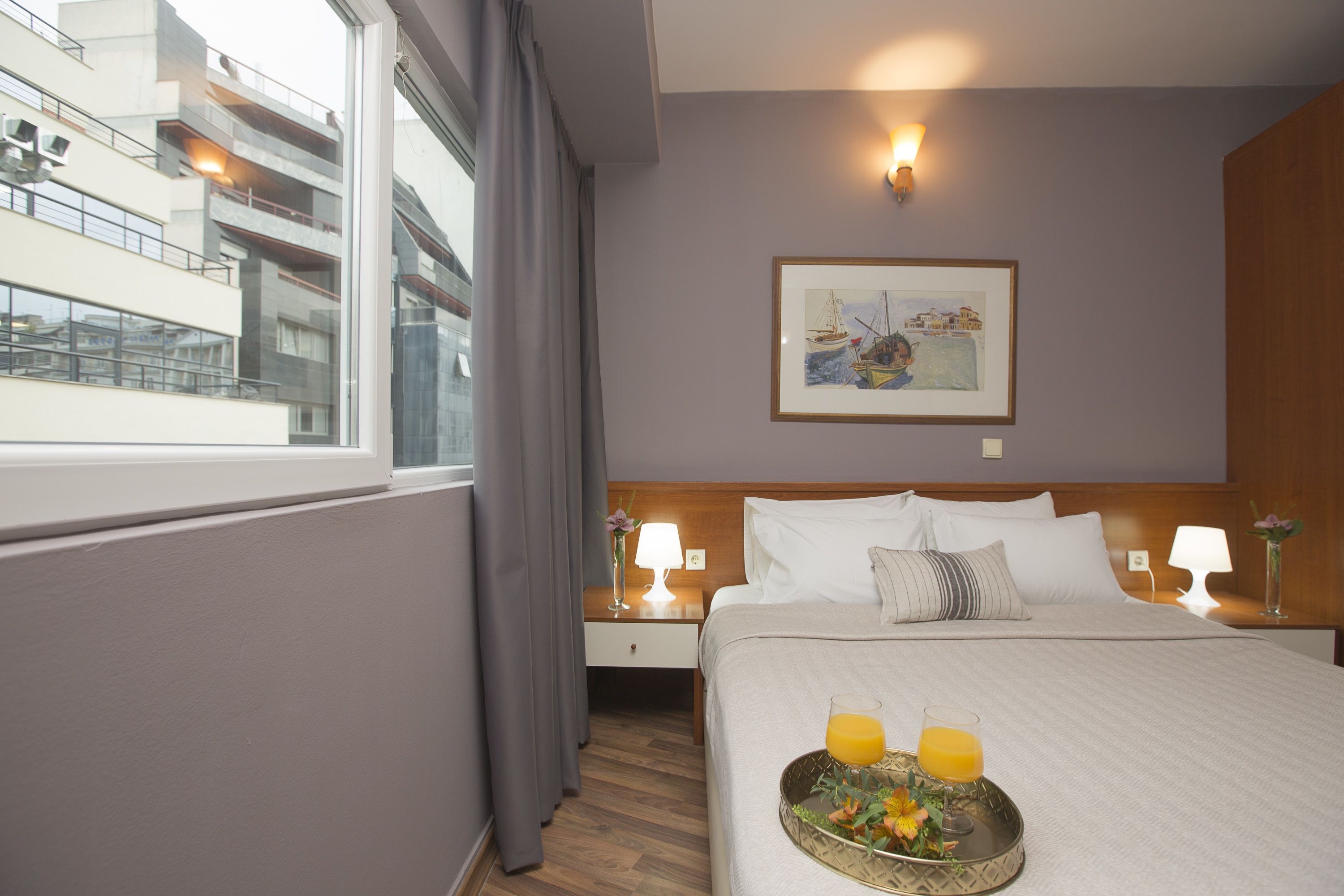 A hotel room with a large bed, a nightstand with a lamp, a framed picture on the wall, and a window with curtains.
