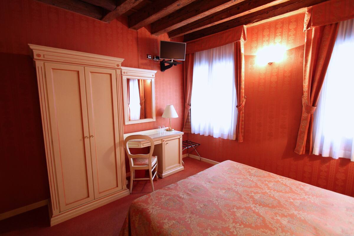 A room with a bed, a desk, a chair, a wardrobe, and a TV mounted on the wall.