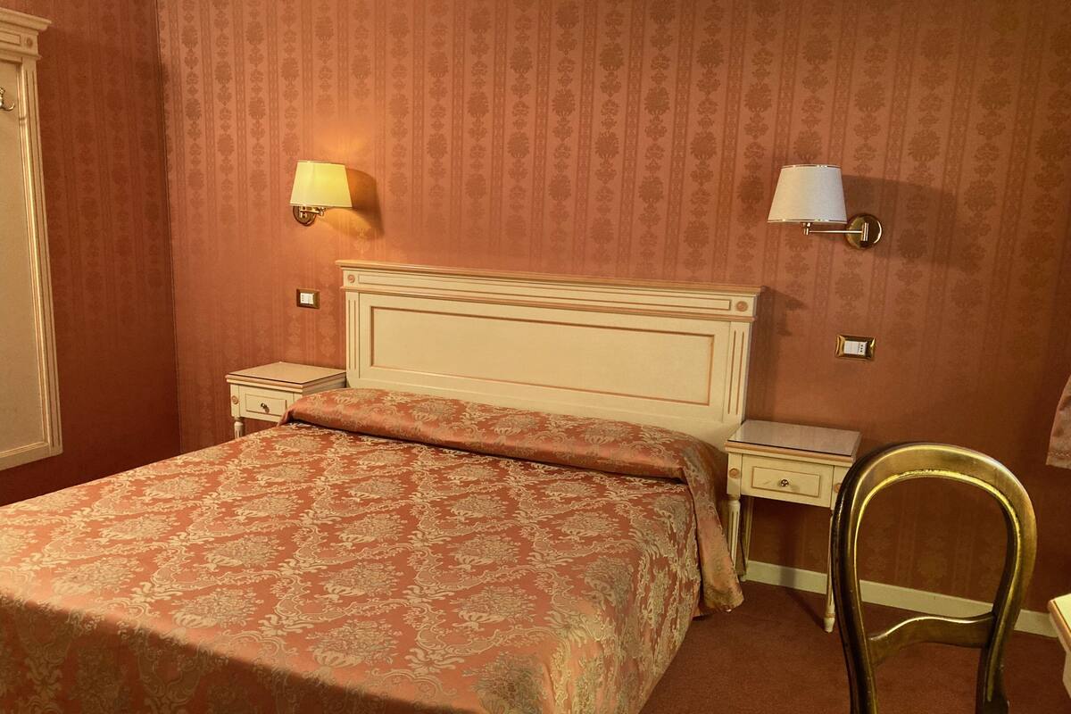 A hotel room with a large bed, two bedside tables, a chair, and two wall-mounted lamps.