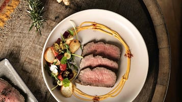 A plate of sliced meat with a side salad and bread on a wooden table.