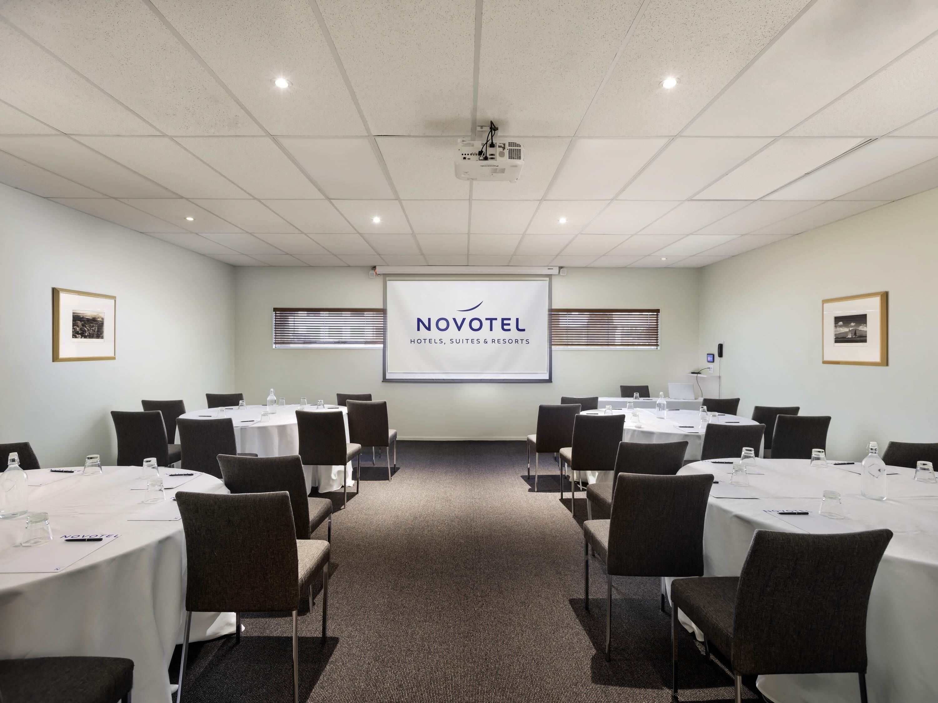 A conference room with multiple tables, chairs, a projector screen, and a presentation on the wall.