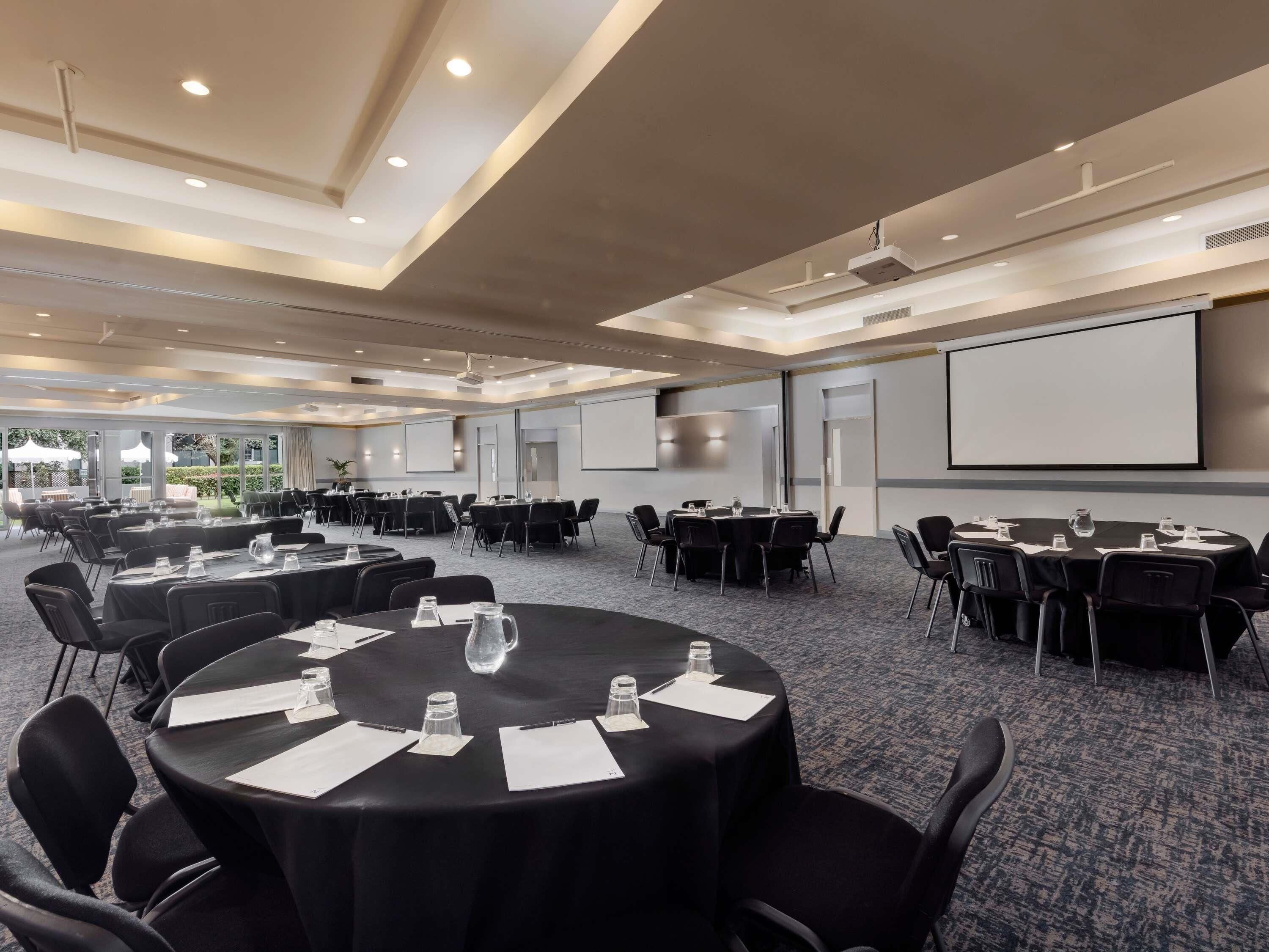 A conference room with round tables, black chairs, and a projector screen.