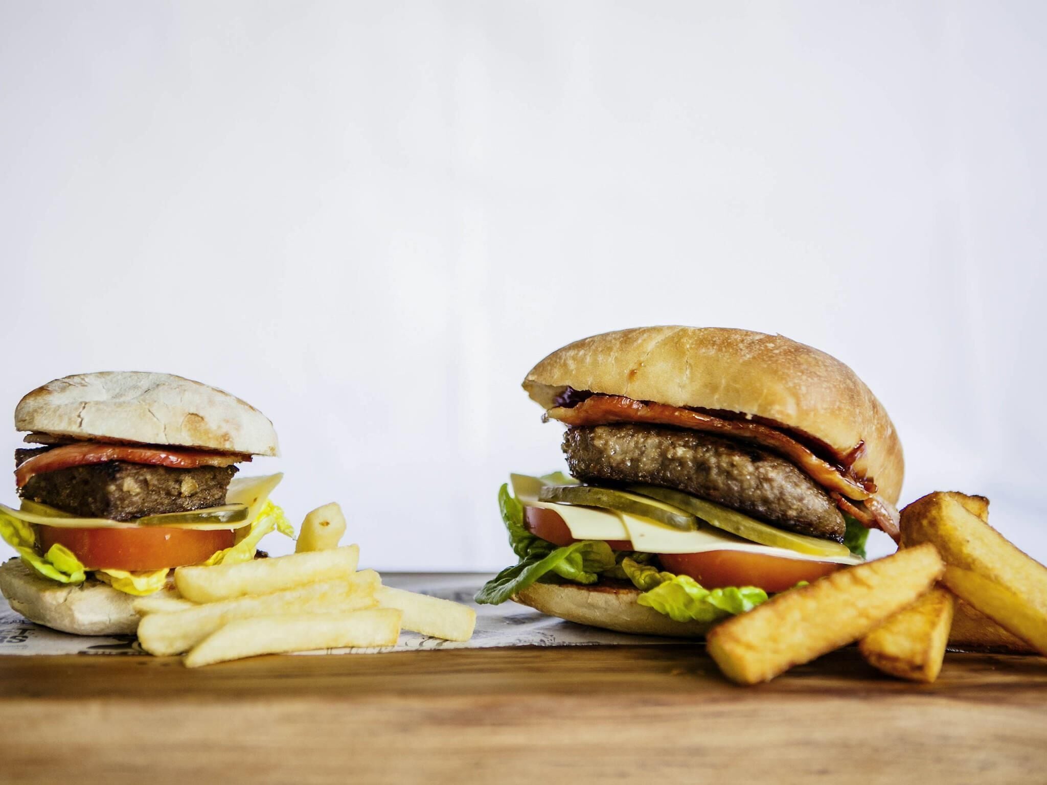 Two burgers with fries on a wooden surface.