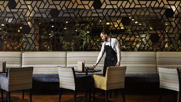 Un restaurante con un diseño moderno de pared geométrica, asientos acolchados y un camarero atendiendo una mesa.