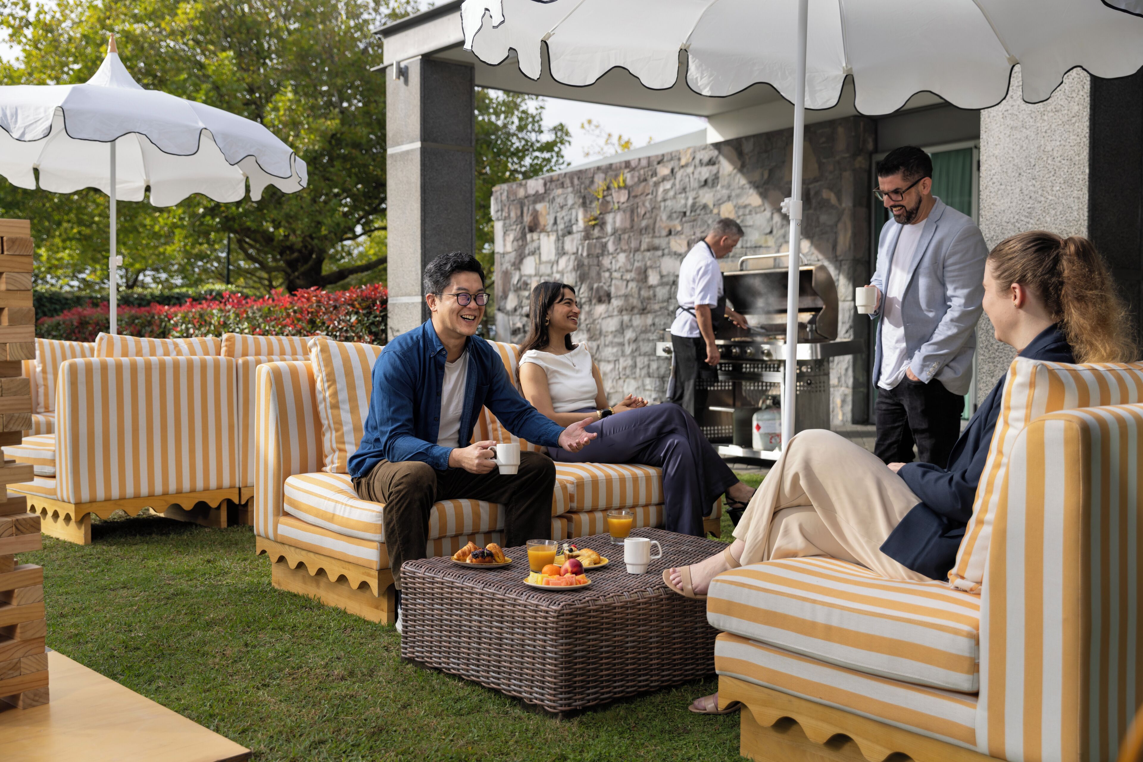 A patio area with striped sofas, a wicker table with food and drinks, and a stone wall in the background.