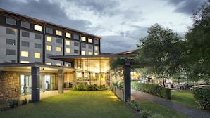 A modern hotel with a well-maintained lawn, outdoor seating area, and a glass facade.