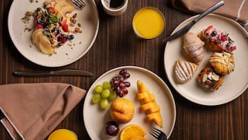 Et morgenbord med tallerkener med mad, en kaffekop og et glas appelsinjuice på et træbord.