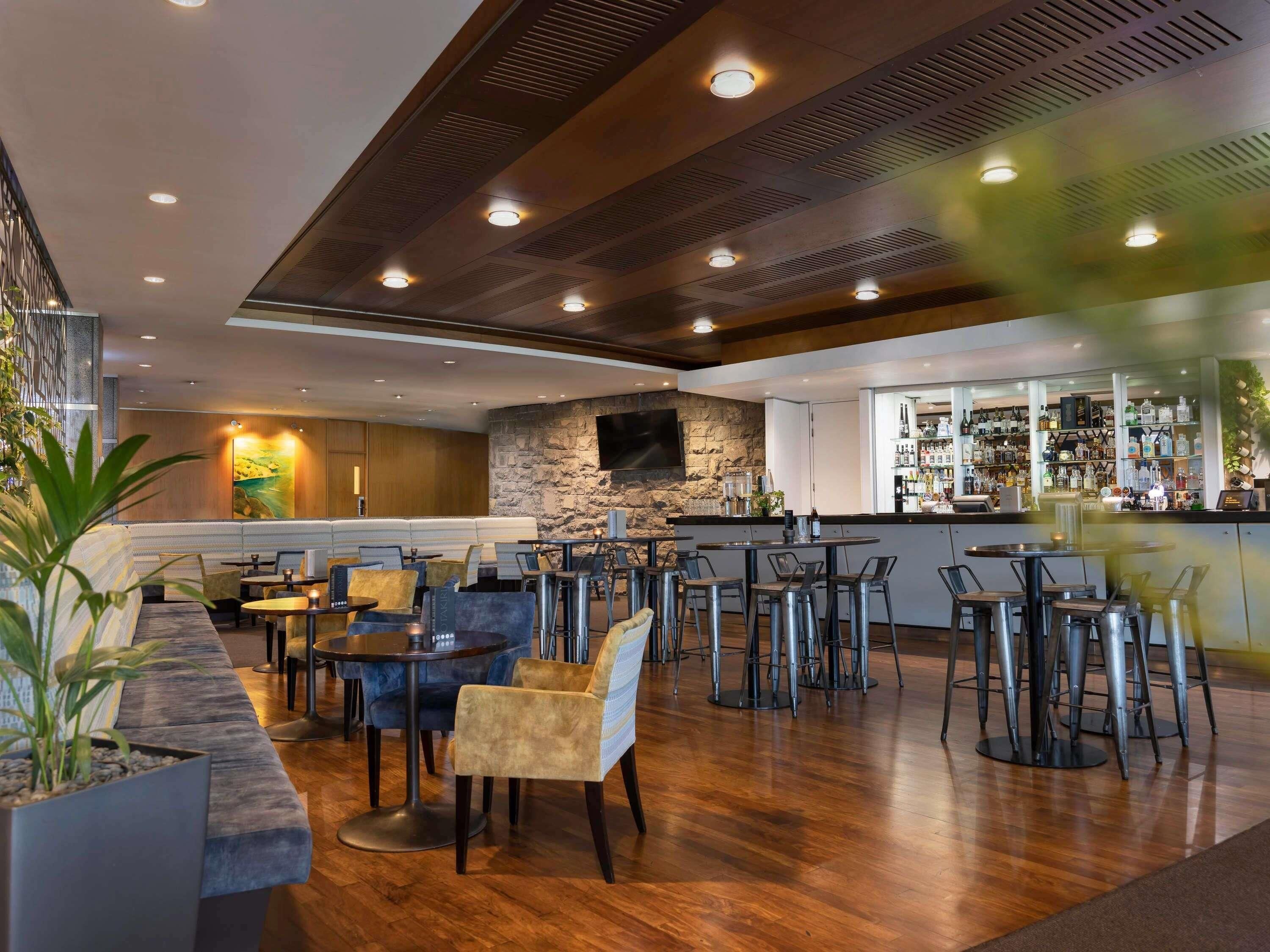 A modern bar area with seating, a stone accent wall, and a bar stocked with various bottles.