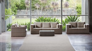 A modern interior with large windows, wicker furniture, and a view of a garden.