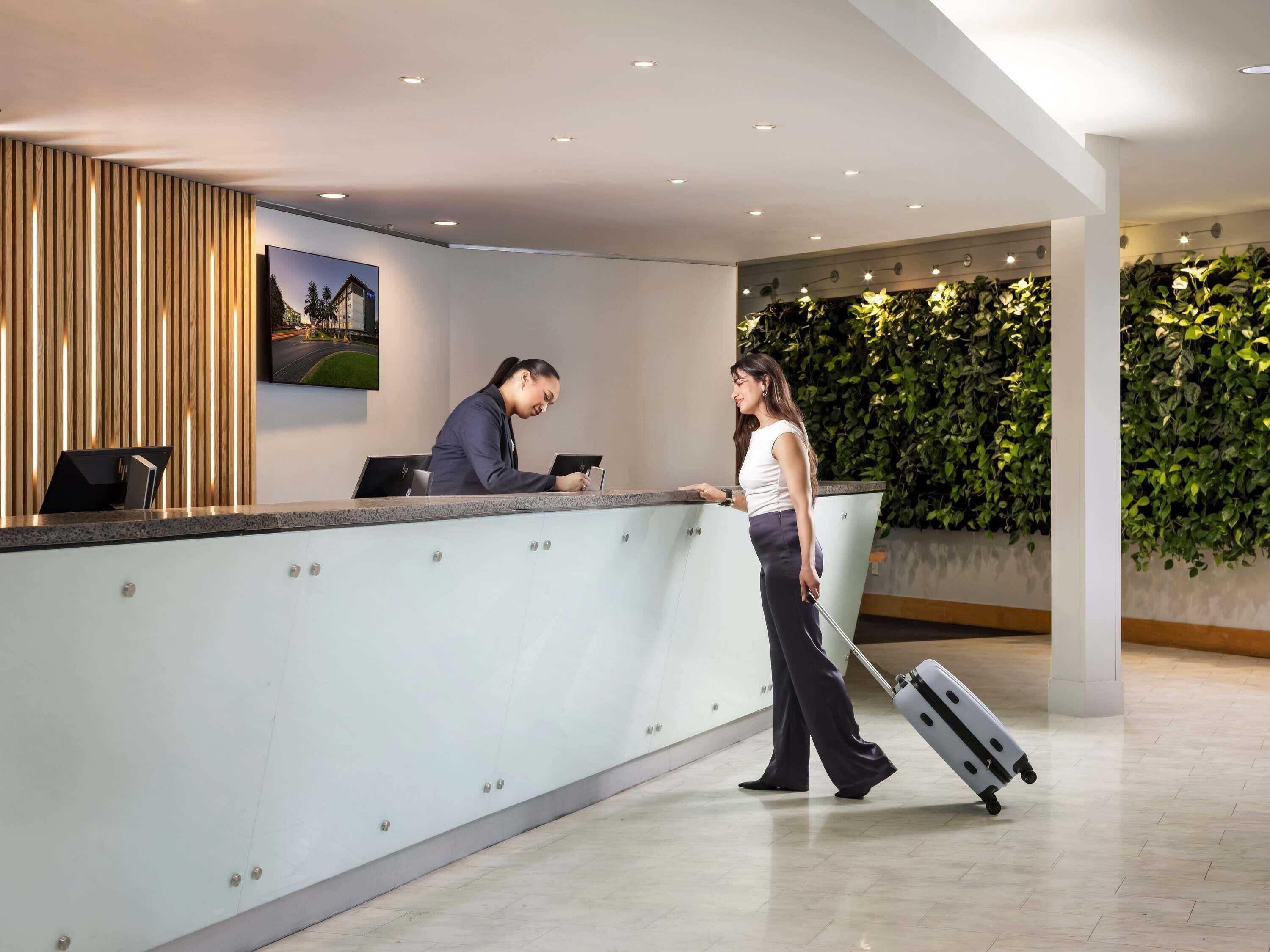 A reception desk with a modern design, a large wall-mounted picture, and a green wall with plants.