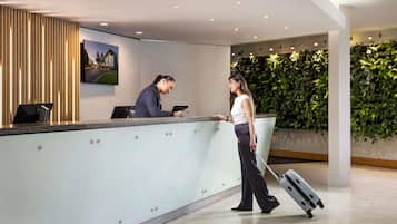 A reception desk with a modern design, a large wall-mounted picture, and a green wall with plants.