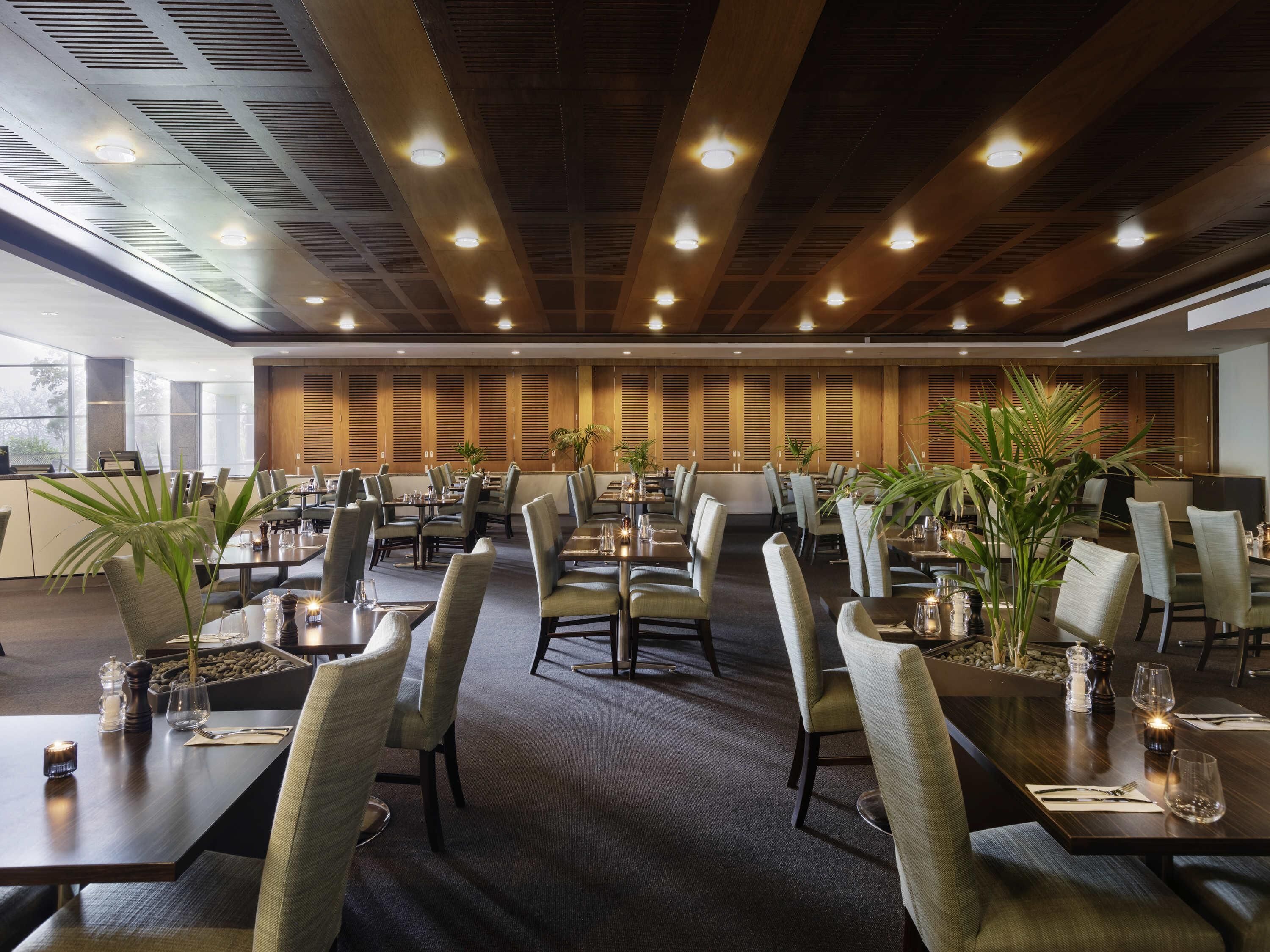 Un grand espace dédié à la salle à manger, avec plusieurs tables et chaises, un mur en bois avec des panneaux à lattes et des luminaires au plafond.