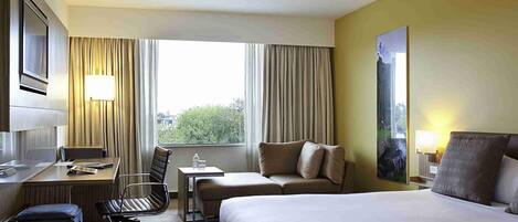 A hotel room with a bed, desk, chair, and a window with curtains.