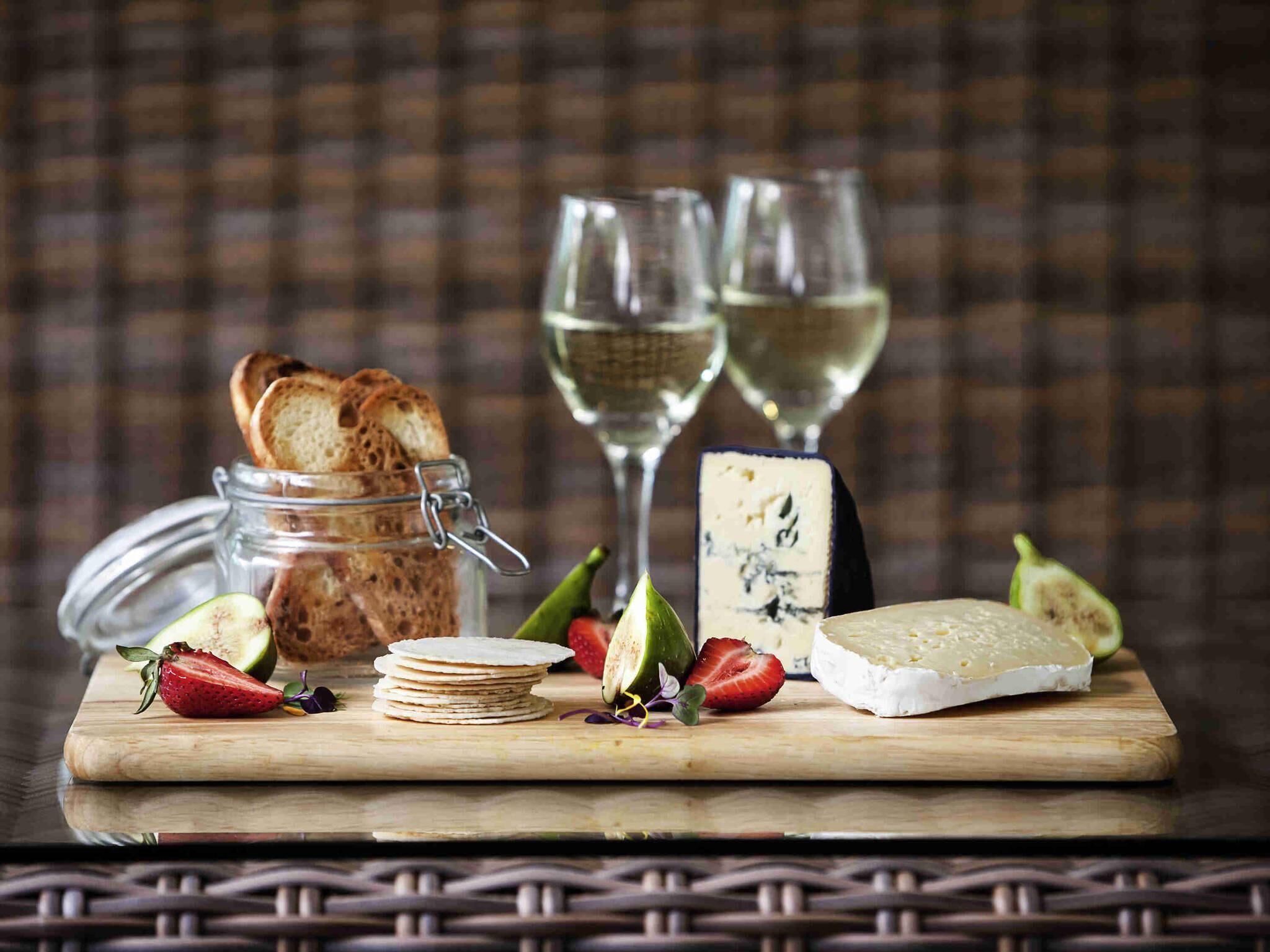 A cheese board with various cheeses, strawberries, and bread on a wooden board, accompanied by glasses of white wine.