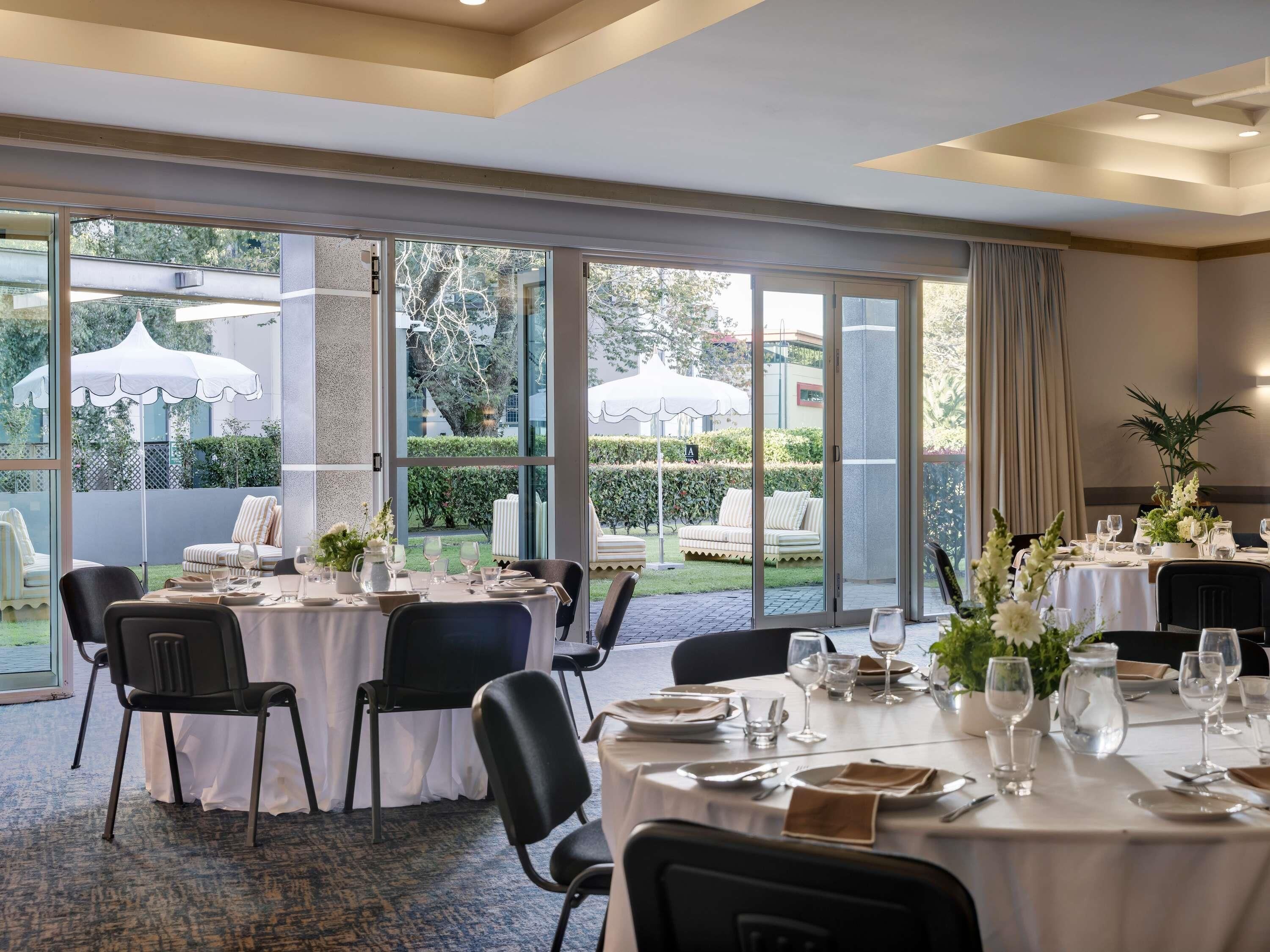 A dining area with tables set for service, large windows, and a view of the outdoors.