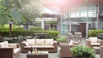 An outdoor seating area with wicker furniture, a potted plant, and a glass building in the background.