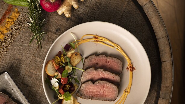 A plate of sliced meat with vegetables and herbs, a tray with additional food items, and a rustic wooden table. - Novotel Auckland Ellerslie (Auckland)