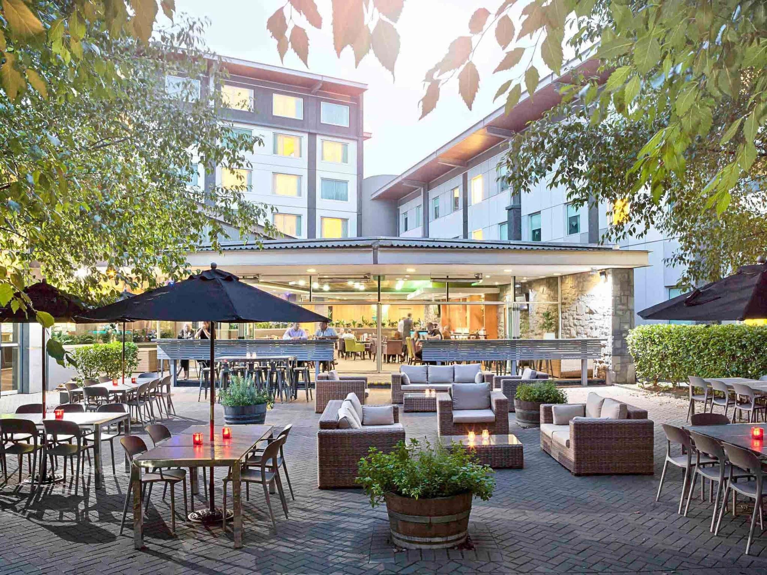 An outdoor patio area with tables and chairs, a covered seating area, and a building in the background.